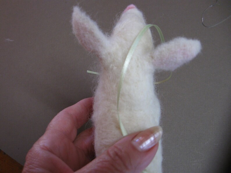 May include: A white felt animal with a pink nose and light green ribbon tied around its body.