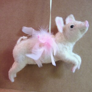 May include: A white pig wearing a pink tutu and white feather wings. The pig is a handmade ornament.