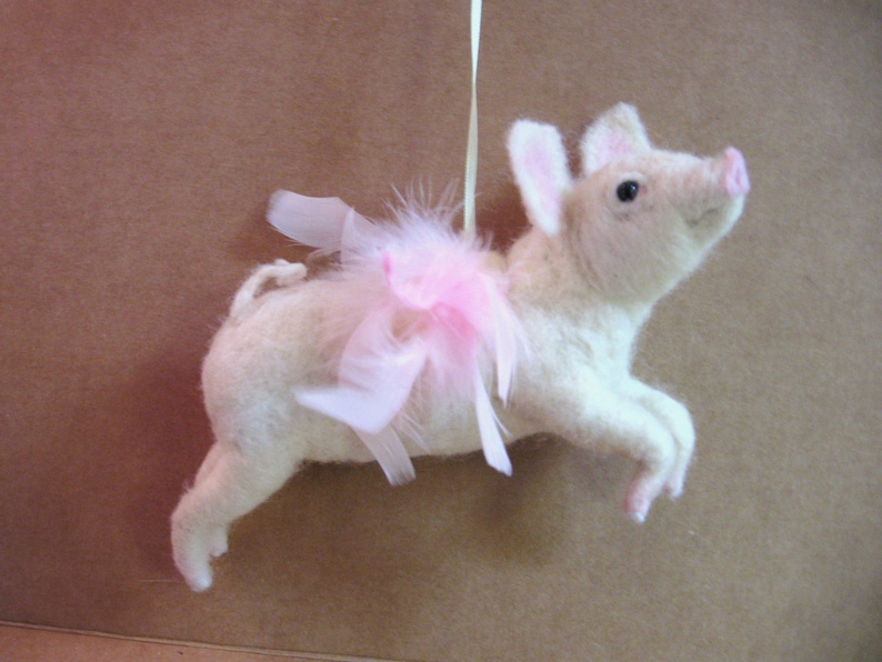 May include: A white pig wearing a pink tutu and white feather wings. The pig is a handmade ornament.