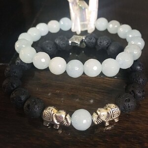 May include: Two bracelets, one made of light blue beads and the other of black lava rock beads, with silver elephant charms.
