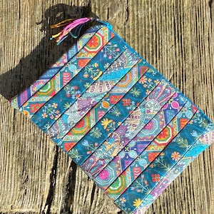 May include: A teal blue zippered pouch with a colourful paisley pattern. The pouch has a pink and yellow tassel.