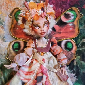 Peut inclure: Une poupée artisanale avec des ailes de papillon, une couronne florale et une robe rose et orange. La poupée tient une petite bouteille en verre.