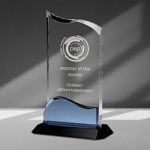 May include: A clear glass award with a blue base and a black base. The award has the text "pepstar of the month" and "October: Allison Lesperance" on it. The award also has a logo with the text "pep" inside a circle.