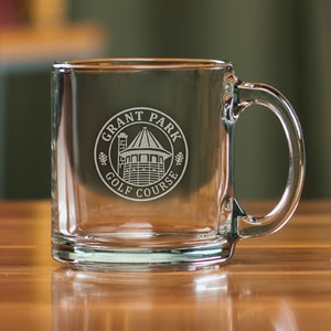 May include: A clear glass mug with a handle. The mug is engraved with a logo that says "Grant Park Golf Course" in a circle with a building inside.