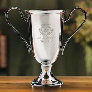 May include: A silver trophy cup with two handles. The cup has an engraved crest with the letters "WG CC" and the text "Club Championship Champion".