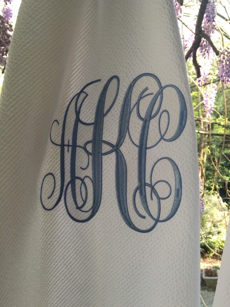 以下が含まれることがあります： 白いワッフル織りの生地に、青い刺繍で「KC」の文字が筆記体で刺繍されています。