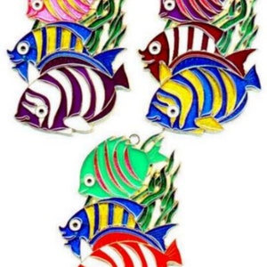 May include: Colorful enamel fish ornaments in pink, purple, blue, yellow, red, and green with white stripes and gold trim. Each fish has a loop for hanging and is set against green seaweed. These decorative ornaments are ideal for nautical or ocean-themed decor.