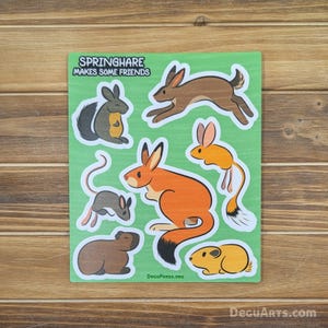 以下が含まれることがあります： さまざまな動物のイラストが描かれた緑色のステッカーシート。スプリングヘア、ウサギ、ジャコウネズミ、マウス、ピッカ、ジャービルなど。シートの上部には「Springhare Makes Some Friends」というテキストがあります。