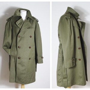 K&ouml;nnte beinhalten: Ein gr&uuml;ner Trenchcoat mit doppeltem Knopfschloss, G&uuml;rtel und braunen Kn&ouml;pfen.