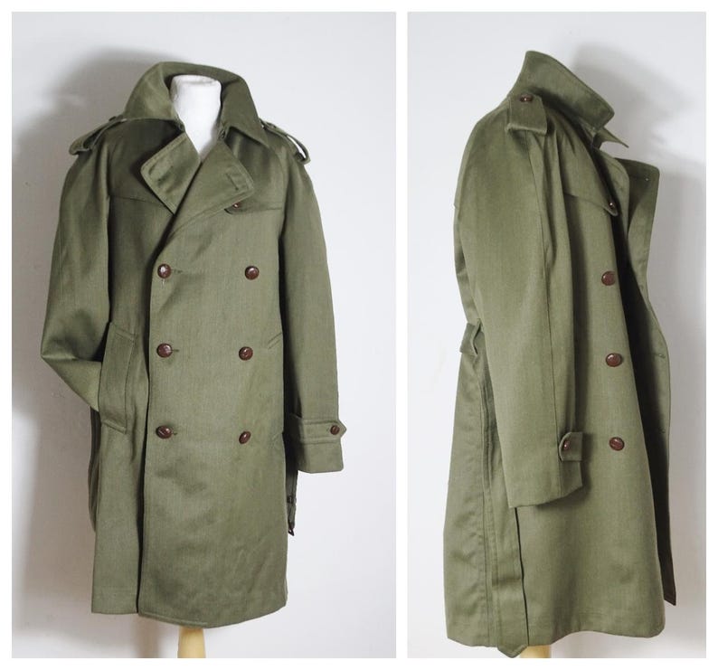 K&ouml;nnte beinhalten: Ein gr&uuml;ner Trenchcoat mit doppeltem Knopfschloss, G&uuml;rtel und braunen Kn&ouml;pfen.