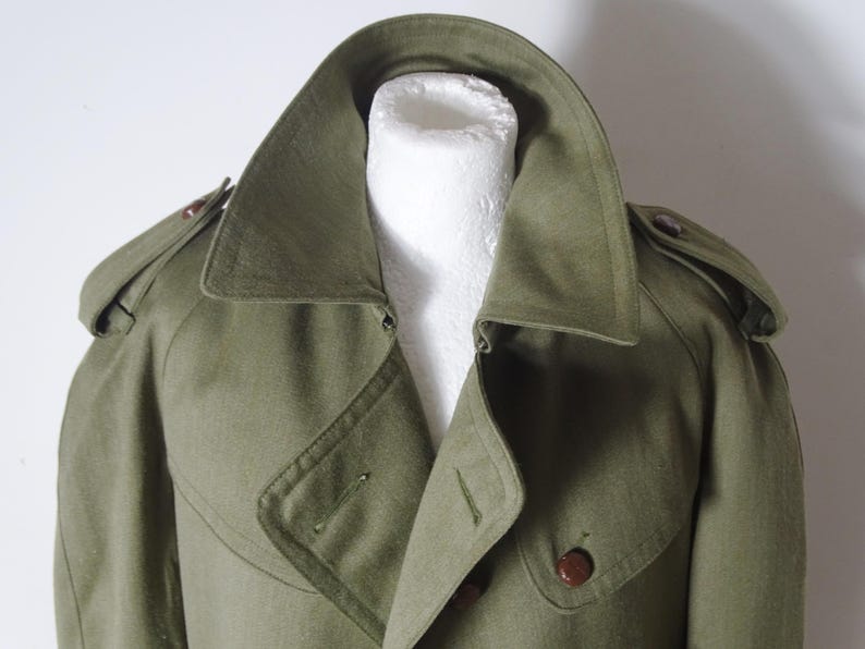 K&ouml;nnte beinhalten: Ein gr&uuml;ner Trenchcoat im Milit&auml;rstil mit doppelreihigem Verschluss und einem gro&szlig;en Kragen.