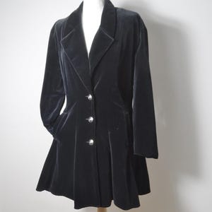 Puede incluir: Un blazer de terciopelo negro con solapa de muesca, mangas largas y dobladillo acampanado. La prenda se abrocha con tres botones plateados en la parte central delantera e incluye dos bolsillos laterales integrados en la falda acampanada.