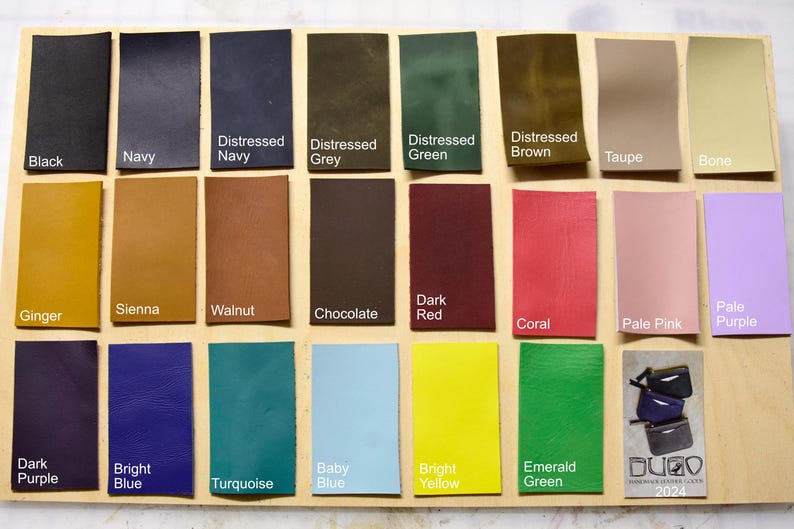 May include: A chart of 24 leather swatches in various colors, including black, navy, distressed navy, distressed grey, distressed green, distressed brown, taupe, bone, ginger, sienna, walnut, chocolate, dark red, coral, pale pink, pale purple, dark purple, bright blue, turquoise, baby blue, bright yellow, emerald green. The chart is labeled with the color names.