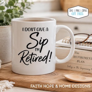 Könnte beinhalten: Weiße Keramiktasse mit dem Text "I DON'T GIVE A Sip I'M Retired!" in schwarzer Schrift. Die Tasse ist mit einer dunklen Flüssigkeit gefüllt und steht auf einer Holzoberfläche. Ein Buch und ein Löffel sind im Hintergrund.