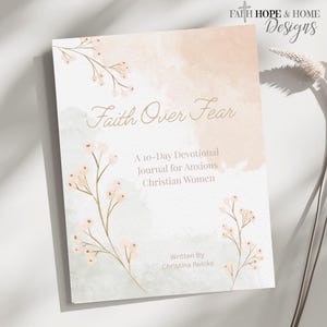 以下が含まれることがあります： 「Faith Over Fear」というタイトルの日記帳で、花のイラストが描かれています。表紙は、桃色と灰色の水彩画風です。「A 10-Day Devotional Journal for Anxious Christian Women」と著者の名前、Christina Reinkeというテキストが含まれています。