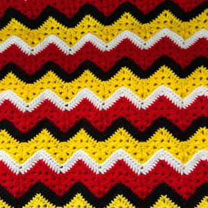May include: A crocheted blanket with a chevron pattern in red, yellow, black, and white.