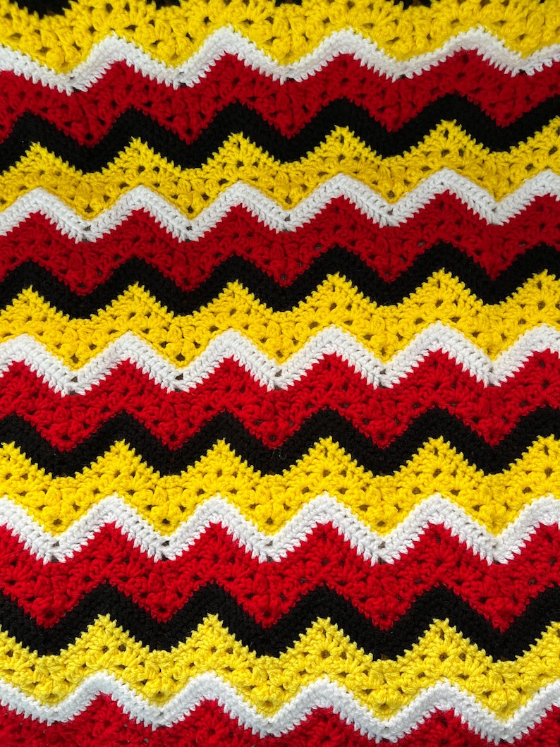 May include: A crocheted blanket with a chevron pattern in red, yellow, black, and white.
