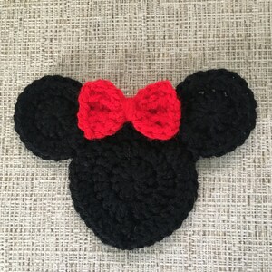May include: A black crocheted mouse head with two round ears and a red bow. The handmade item is likely a decorative piece or part of a larger craft project. The design is reminiscent of a popular cartoon character.