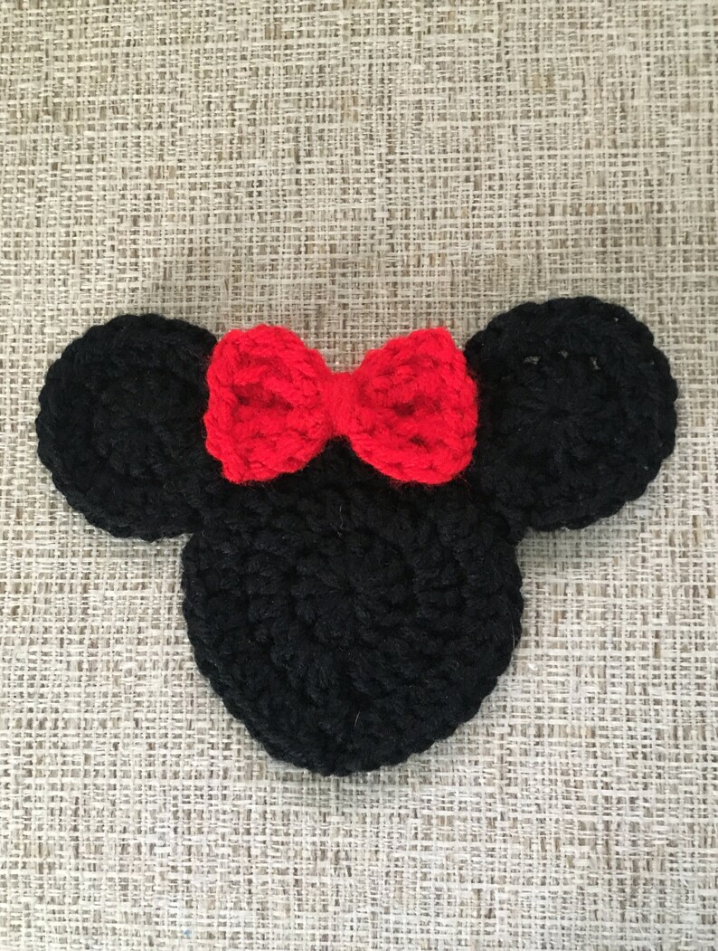 May include: A black crocheted mouse head with two round ears and a red bow. The handmade item is likely a decorative piece or part of a larger craft project. The design is reminiscent of a popular cartoon character.