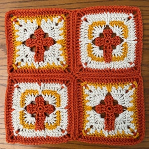 May include: Four crocheted squares in orange, white, and yellow, joined together to form a larger square. Each square features a central flower design.
