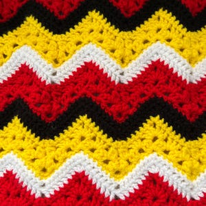 May include: A crocheted blanket with a chevron pattern in red, yellow, black and white.