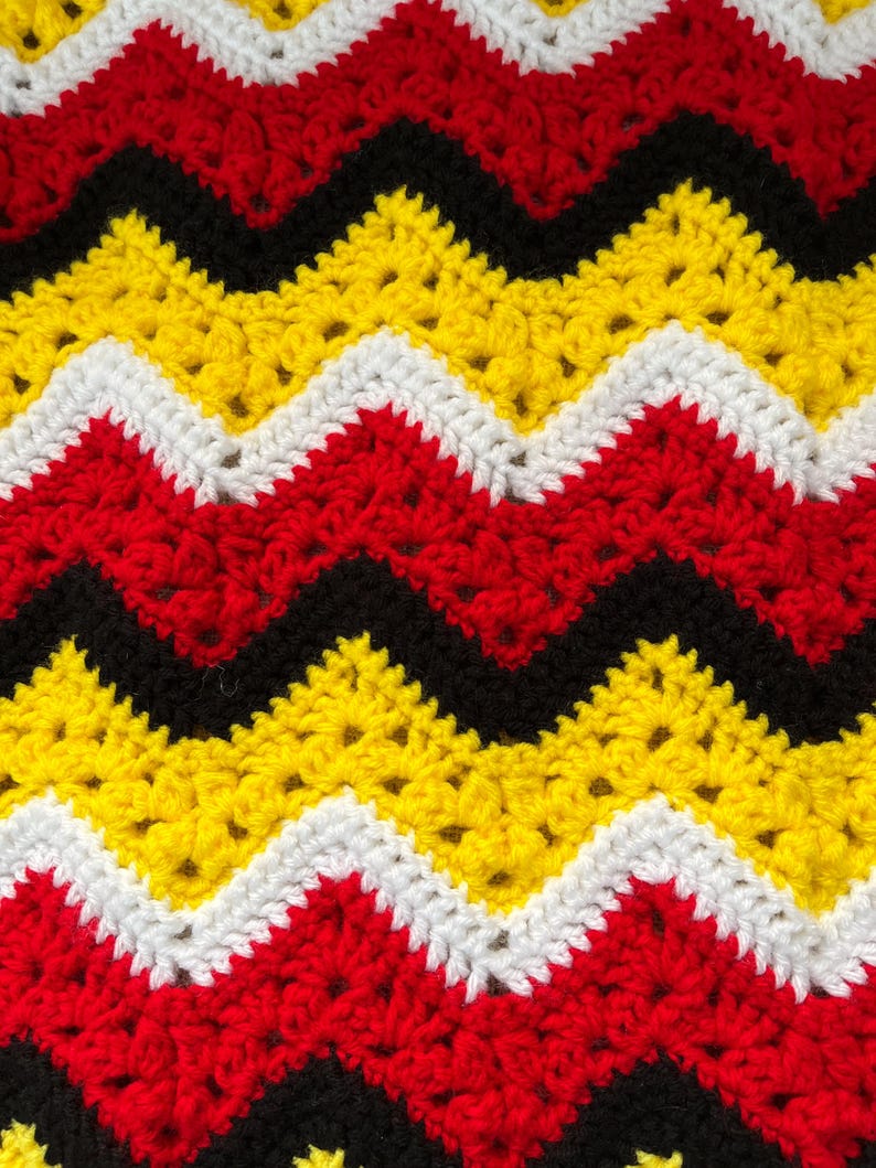 May include: A crocheted blanket with a chevron pattern in red, yellow, black and white.