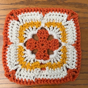 May include: A crocheted square with a flower design in orange, yellow, and white.