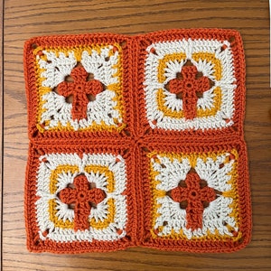 May include: Four crocheted squares in orange, white, and yellow, joined together to form a larger square.
