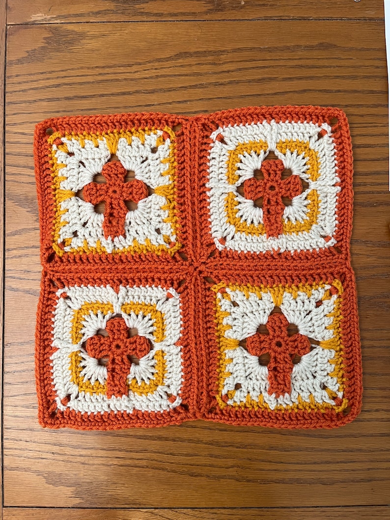 May include: Four crocheted squares in orange, white, and yellow, joined together to form a larger square.