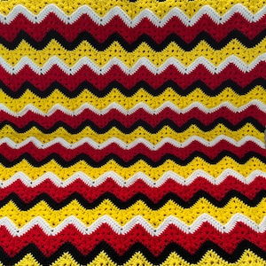 May include: A crocheted blanket with a chevron pattern in red, yellow, black, and white.