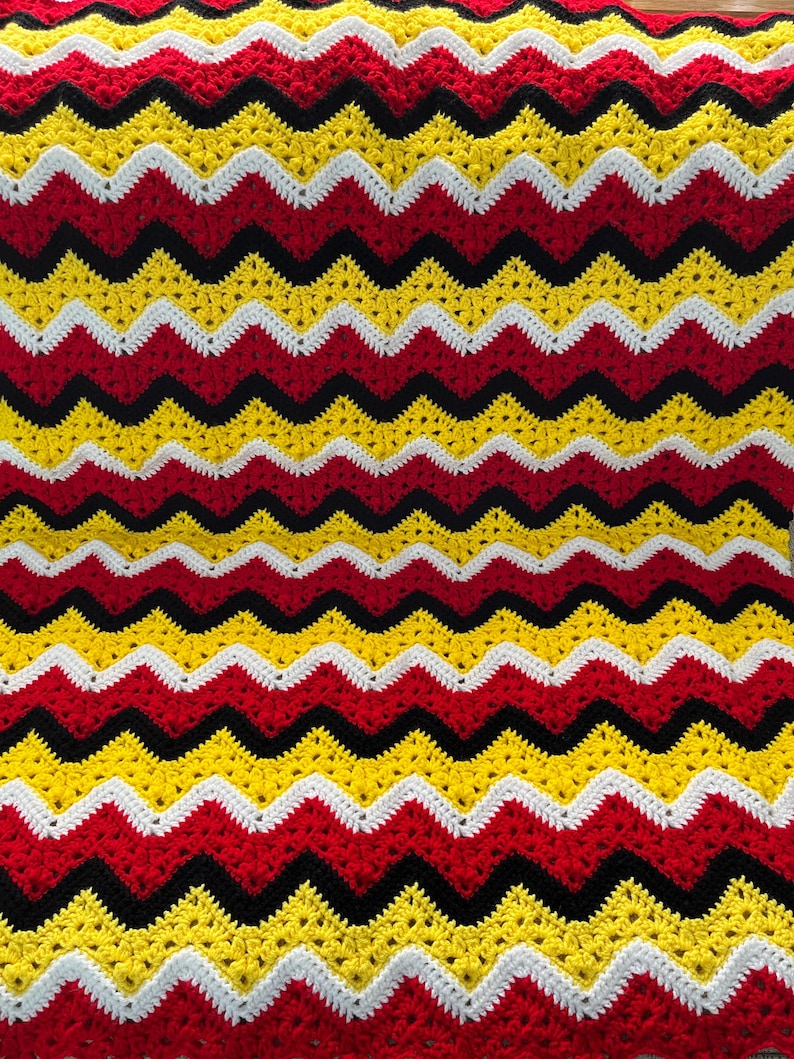 May include: A crocheted blanket with a chevron pattern in red, yellow, black, and white.