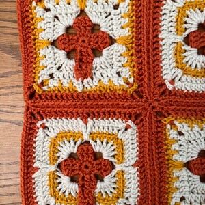 May include: Two crocheted squares with a flower design in the center. The squares are made with orange, white, and yellow yarn.