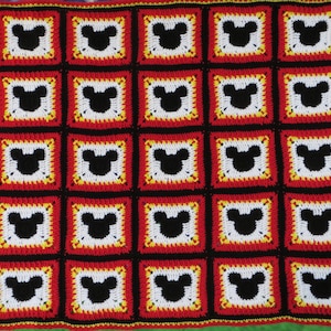 May include: A crocheted blanket featuring a repeating pattern of Mickey Mouse heads in black, white, red and yellow.