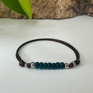 May include: A brown cord bracelet with a row of dark teal glass beads and silver metal beads.