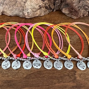 May include: A set of 12 colorful friendship bracelets with silver bird charms. The bracelets are made with thin cord and feature a variety of bright colors, including orange, yellow, pink, and red.