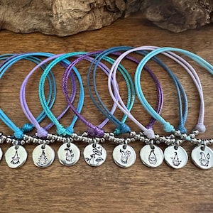 May include: Eight colorful friendship bracelets with silver charms featuring different gnome and mushroom designs. The bracelets are made with a variety of shades of blue, purple, and teal.
