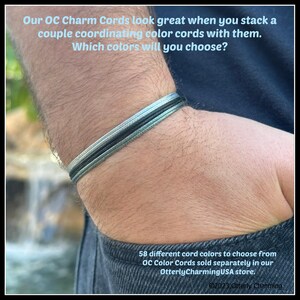 K&ouml;nnte beinhalten: Ein Set aus drei d&uuml;nnen, geschichteten Kordelarmb&auml;ndern in den Farben Hellblau, Dunkelgrau und Schwarz. Der Text auf dem Bild lautet: Our OC Charm Cords look great when you stack a couple coordinating color cords with them. Which colors will you choose?