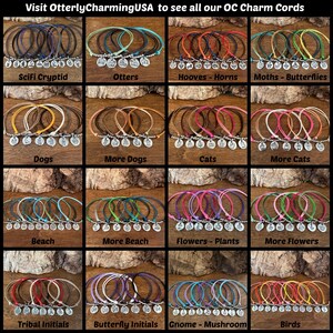K&ouml;nnte beinhalten: Eine Sammlung von sechzehn Sets aus farbigen Kordelarmb&auml;ndern, die jeweils mit einem silberfarbenen Metallanh&auml;nger versehen sind. Die Themen umfassen Sci-Fi-Kryptiden, Otter, Hufe, Motten, Hunde, Katzen, Strand, Blumen, Pflanzen und V&ouml;gel.