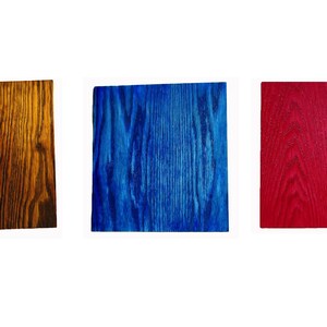 May include: Five wood samples stained in different colors: black, brown, blue, red, and natural wood.