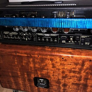 May include: A black amplifier head with a blue wood panel on the front. The amplifier is sitting on top of a wooden cabinet with a speaker.