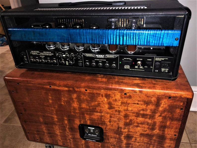 May include: A black amplifier head with a blue wood panel on the front. The amplifier is sitting on top of a wooden cabinet with a speaker.