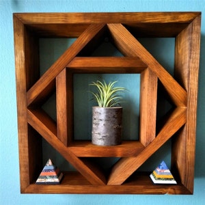 May include: A wooden geometric shelf with three shelves. The top shelf has a small potted plant, the bottom two shelves have decorative items. The shelf is stained a dark brown color.