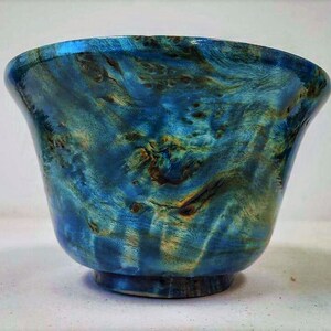 May include: A blue and green wooden bowl with a swirling grain pattern. The bowl is made of wood and has a smooth, polished finish.