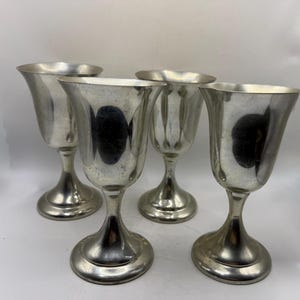 May include: Four silver-colored goblets with a flared rim and a rounded base. The goblets have a reflective surface and are arranged in a group, suggesting a set. The stem is slender, and the base is wide, providing stability.
