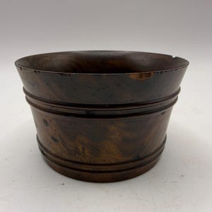 May include: A dark brown wooden bowl with a smooth, polished finish and visible natural wood grain patterns. The bowl features a wide, open top with a slightly flared rim and two horizontal grooved rings encircling the exterior side walls.