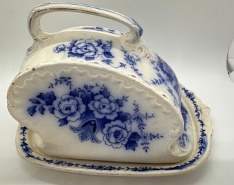 May include: A white ceramic cheese dish with a blue and white floral pattern. The dish has a handle and a separate base.