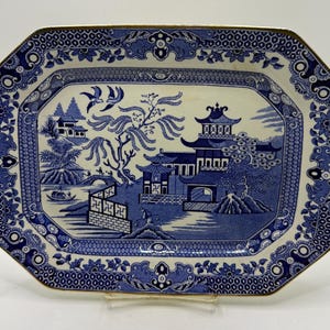 May include: An octagonal ceramic platter featuring a blue and white willow pattern. The central design depicts a landscape with pagodas, a willow tree, two birds, a bridge, and a boat. The border is decorated with intricate geometric and floral motifs.
