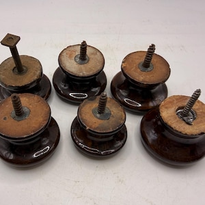 Pode incluir: Um conjunto de cinco puxadores redondos de cer&acirc;mica castanho-escuro com acabamentos brilhantes. Cada puxador apresenta uma base plana de madeira clara e um mecanismo de parafuso ou perno de metal que sobressai do centro para fixa&ccedil;&atilde;o.