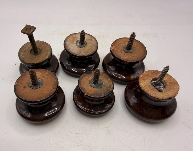 Pode incluir: Um conjunto de cinco puxadores redondos de cer&acirc;mica castanho-escuro com acabamentos brilhantes. Cada puxador apresenta uma base plana de madeira clara e um mecanismo de parafuso ou perno de metal que sobressai do centro para fixa&ccedil;&atilde;o.