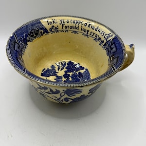 May include: Antique blue and yellow ceramic bowl with a handle. The bowl features a blue and white floral pattern and a rim with text that reads "Tak ye a cuppo kindness For auld lang syne."
